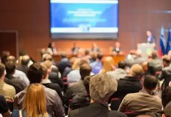 Ejecutivos sentados en una convención, todos de espaldas viendo hacia la pantalla 