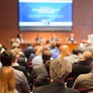 Ejecutivos sentados en una convención, todos de espaldas viendo hacia la pantalla 